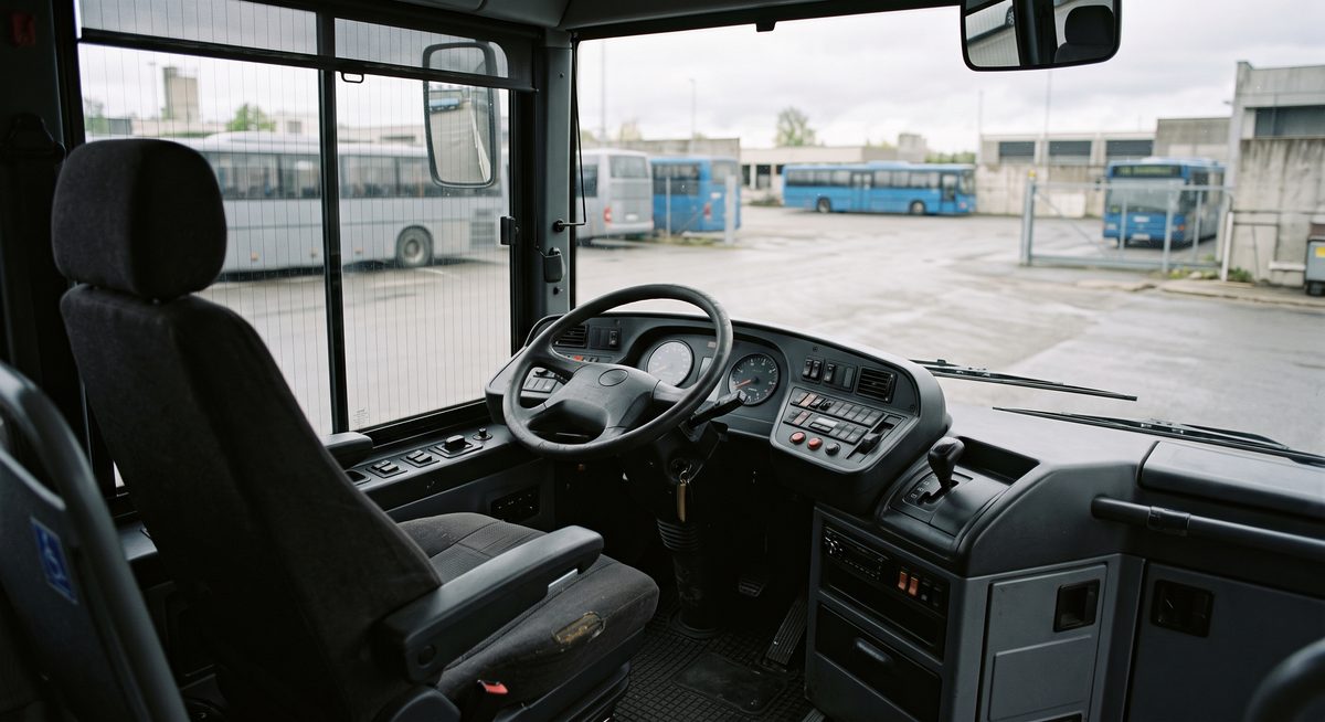 Leerer Fahrerplatz eines Reisebusses mit Lenkrad und Armaturen, Blick auf einen Betriebshof.